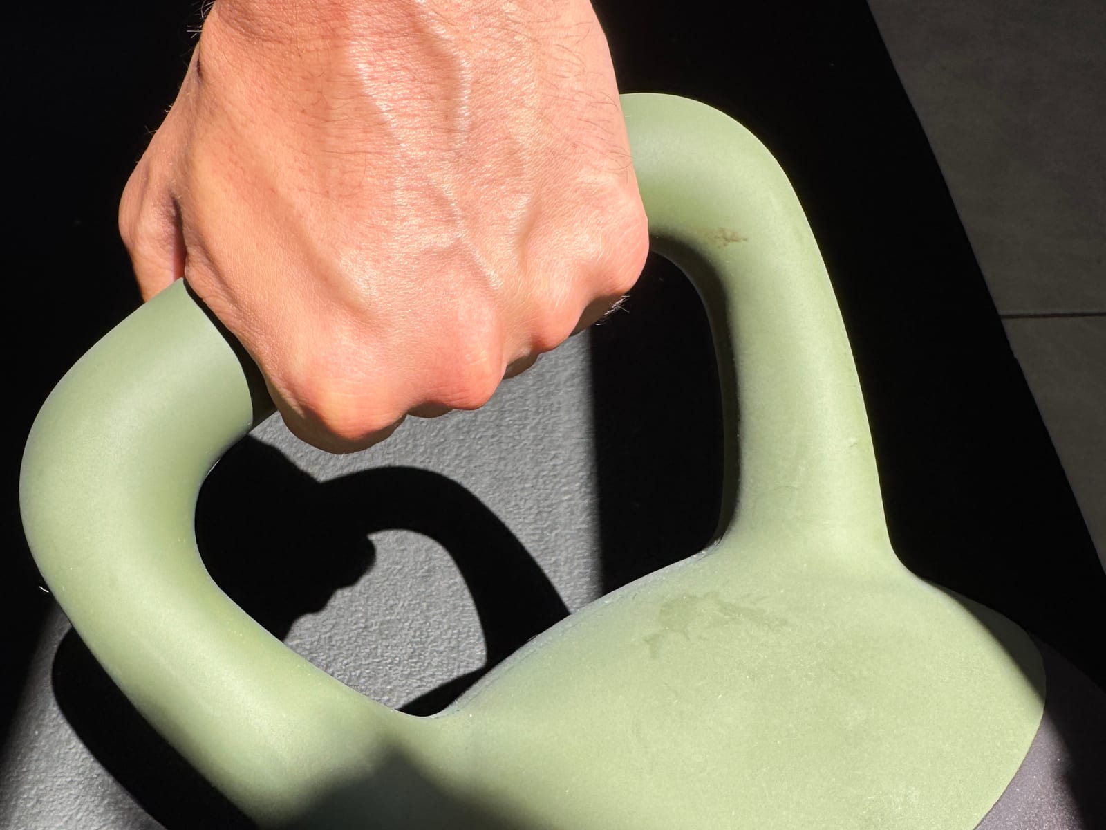 Hand gripping a kettlebell handle in hard side light